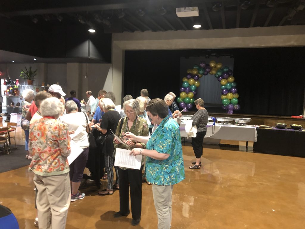 Group of people socializing in a room with a balloon arch in the background, enjoying refreshments.